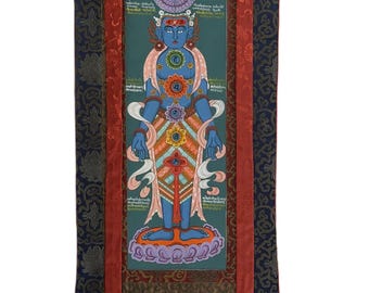 May include: A vertical, ornate wall hanging featuring a central image of a blue deity with multiple arms and colorful floral accents. The artwork is framed by a dark blue fabric with a gold floral pattern, red trim, and a gold top.
