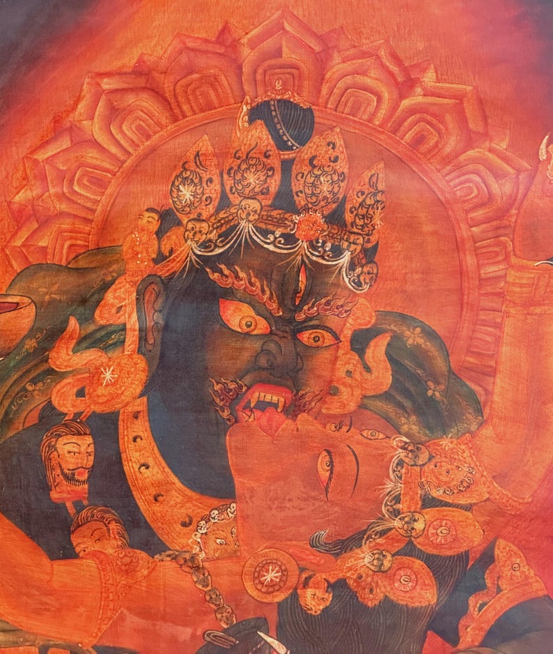 May include: A detailed painting featuring a dark-skinned deity with a fierce expression, bared teeth, and a third eye, embracing a lighter-skinned figure. The artwork is rendered in shades of red and orange, with a lotus-shaped halo background.