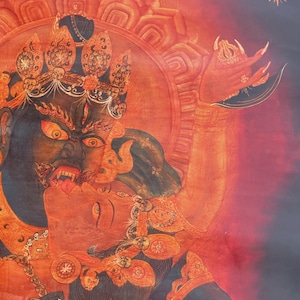 May include: A detailed thangka painting featuring a dark-skinned deity with a fierce expression, wearing an ornate crown and jewelry, embracing a red-skinned figure. The artwork uses vibrant shades of red, orange, and black with intricate line work.
