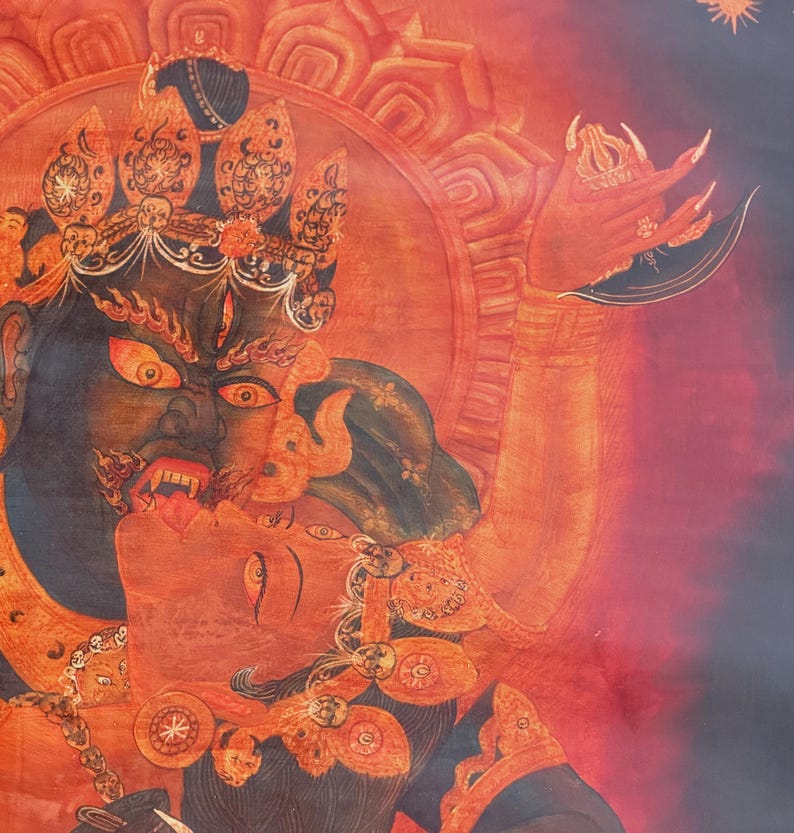May include: A detailed thangka painting featuring a dark-skinned deity with a fierce expression, wearing an ornate crown and jewelry, embracing a red-skinned figure. The artwork uses vibrant shades of red, orange, and black with intricate line work.