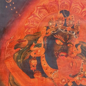 May include: A vibrant painting featuring a dark blue deity with a fierce expression, sharp teeth, and wide eyes, embracing a red figure. The deity wears an ornate crown and jewelry, holding a bowl. The background is a fiery orange with a crescent moon.