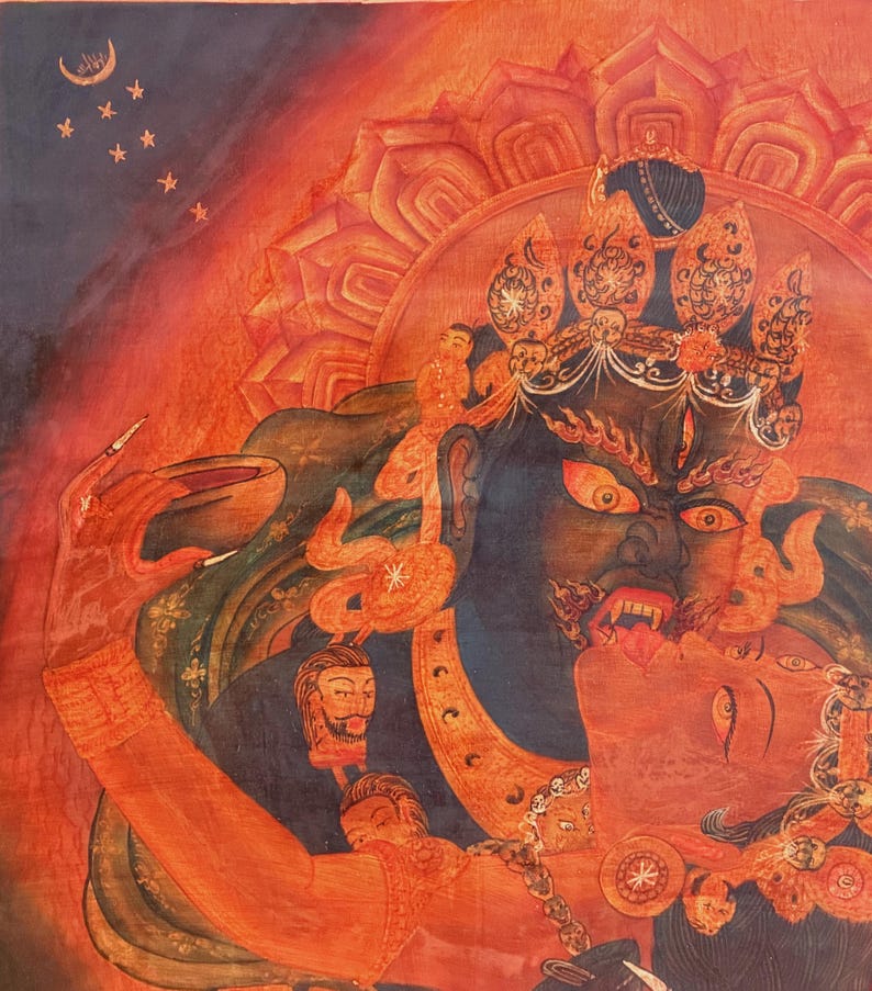 May include: A vibrant painting featuring a dark blue deity with a fierce expression, sharp teeth, and wide eyes, embracing a red figure. The deity wears an ornate crown and jewelry, holding a bowl. The background is a fiery orange with a crescent moon.