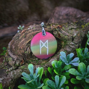 May include: A round pendant with a silver bail and a green, pink, and white layered design. The pendant features a silver rune symbol, the Algiz rune, which represents protection and guidance.