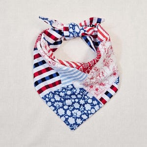 May include: A triangular pet bandana featuring a patchwork design of red, white, and blue patterns. The fabric includes sections of blue and white floral prints, red and white stripes, blue and white gingham checks, and red paisley motifs.