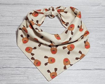 May include: A cream-colored bandana with a repeating pattern of brown reindeer faces with red noses. The bandana is tied in a knot at the top.
