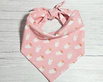 Puede incluir: Un pañuelo triangular para mascotas de color rosa suave con un patrón repetitivo de fantasmas blancos que llevan sombreros de vaquero naranjas. El accesorio de tela se ata en la parte superior con dos extremos para sujetarlo al cuello.