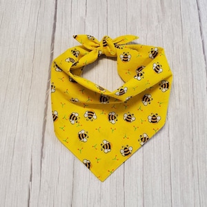 May include: Yellow bandana with a bee pattern. The bandana is tied in a knot at the top and has a triangular shape.