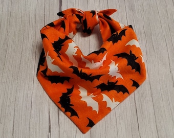 May include: Orange and black bandana with a pattern of white bats. The bandana is tied in a knot at the top.