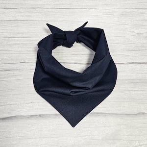May include: A navy blue bandana, folded and tied into a knot, is shown against a white wood background.