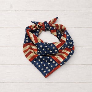 Könnte beinhalten: Ein patriotisches Bandana mit dem Design der amerikanischen Flagge. Der Stoff hat einen Used-Look mit roten und weißen Streifen und einem blauen Feld mit weißen Sternen. Es ist oben gebunden.