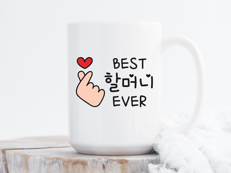 May include: White ceramic mug with a black and white design that says "Best  하얘니  Ever" with a red heart and a pink hand making a heart sign.