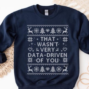 May include: Navy blue sweatshirt with a white knit design. The design includes reindeer, snowflakes, Christmas trees, and hearts. The text reads "THAT WASN'T VERY DATA-DRIVEN OF YOU."