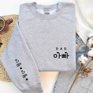 May include: Gray sweatshirt with the word "DAD" and the Korean word for "Dad" written in black text. The left sleeve has the Korean word for "I love you" written in black text.