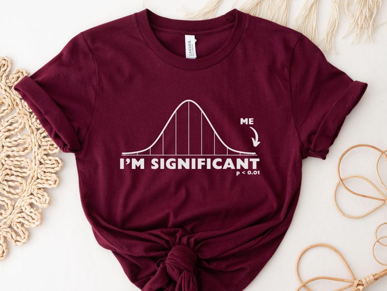 Puede incluir: Camiseta burdeos con un gr&aacute;fico de curva de campana blanca y el texto "I'M SIGNIFICANT p < 0.01". La palabra "ME" est&aacute; al lado de una flecha que apunta a la curva de campana. La camiseta es de material suave.