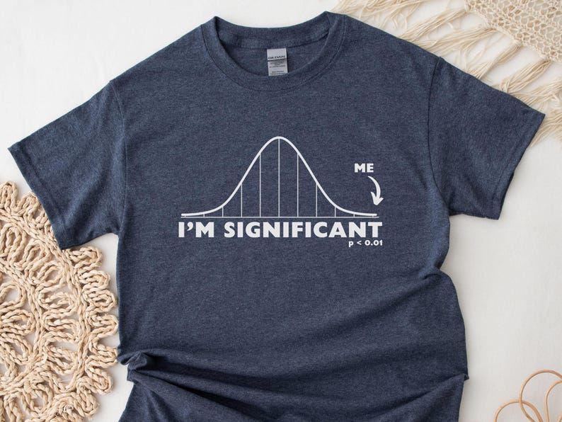 Puede incluir: Camiseta azul marino oscuro con un gr&aacute;fico de curva de campana blanca y el texto "I'M SIGNIFICANT" con "p < 0.01". La palabra "ME" est&aacute; encima de una flecha que apunta a la curva. Una camiseta informal para cient&iacute;ficos.