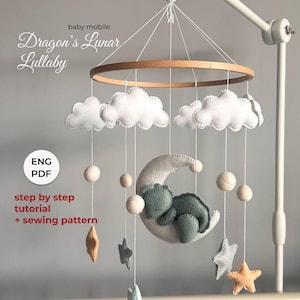 May include: A baby mobile with a wooden ring, felt clouds, stars, and spheres. A felt moon holds a sleeping green dragon. The text "Dragon's Lunar Lullaby" is displayed above. Includes a step-by-step tutorial and sewing pattern.