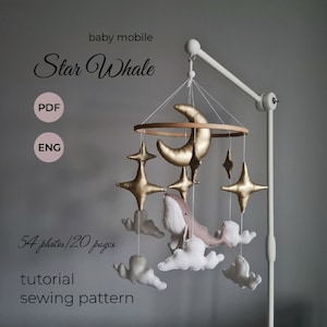 May include: A baby mobile with a celestial theme. It features a gold crescent moon, star shapes, and a whale, along with white clouds. The text on the mobile reads "Star Whale", "baby mobile", "PDF", "ENG", "54 photos/120 pages", "tutorial", and "sewing pattern".
