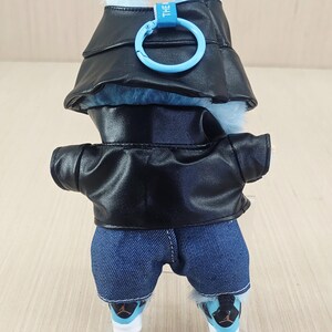 May include: A plush toy wearing a black faux leather jacket, denim shorts, and trainers. The toy has a blue fur head with a matching hat and a blue ring clip. The trainers have black and blue accents.