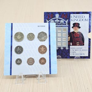 May include: A 1994 United Kingdom coin collection, presented on a light blue card with blue stripes. The collection includes various coins, such as a 50-pence piece. The packaging features an image of a Beefeater and the words 'Brilliant Uncirculated Coin Collection'.