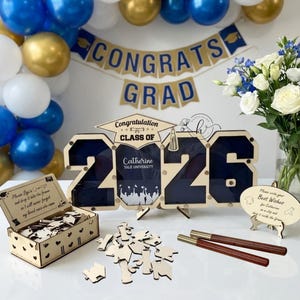 May include: A graduation party decoration set with blue, gold, and white balloons, a banner reading "CONGRATS GRAD," and a wooden sign with "CLASS OF 2026" and a name. Includes a box for guest signatures and pens.