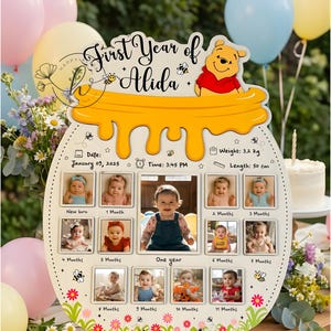 May include: A wooden photo display shaped like a honey pot, featuring a Winnie the Pooh design and the text "First Year of Alida." It includes spaces for 12 photos, with the baby's weight at 7 pounds and length at 19.7 inches. Decorated with flowers and bees.
