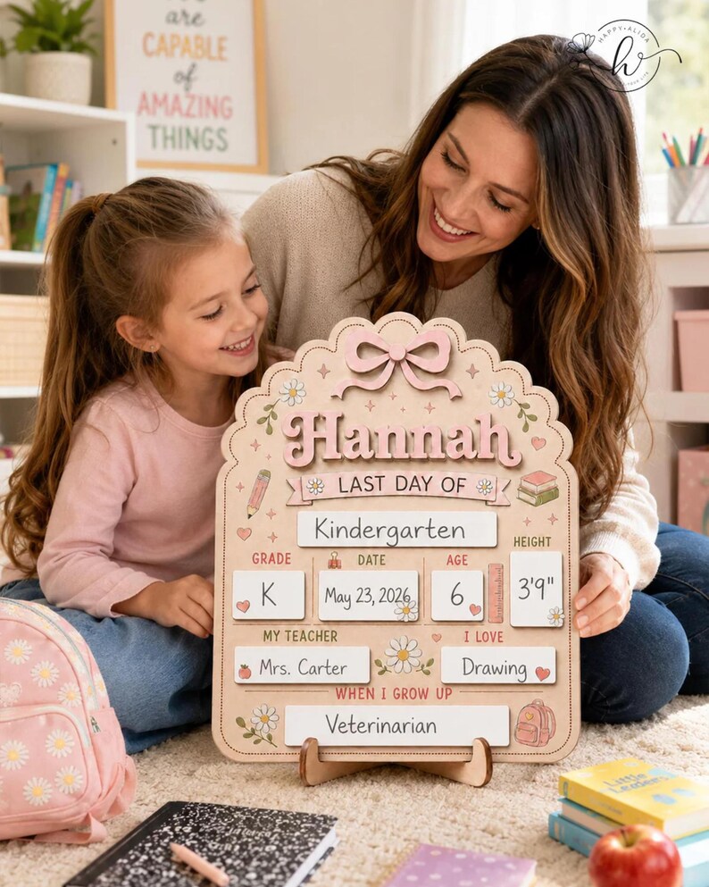 May include: A light-colored wooden sign with a scalloped edge and a pink bow at the top. The text reads "Hannah" and "LAST DAY OF". It includes fields for "Kindergarten", "K", "May 23, 2026", "6", "3'9"", "Mrs. Carter", "Drawing", and "Veterinarian".