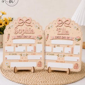 May include: Two light-colored wooden signs for the first day of school, each featuring a scalloped top with a bow, daisy accents, and illustrations of a pencil, books, and backpack. The signs are personalized with the names Sophia and Ella.