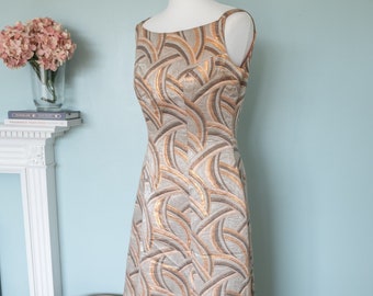 May include: A long, sleeveless, gold and brown patterned dress with a scoop neck. The dress is made of a brocade fabric and has a fitted bodice and a flowing skirt.