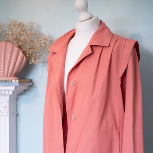 a pastel pink, bomber jacket with collar and shoulder detailing is styled on a manneqin.