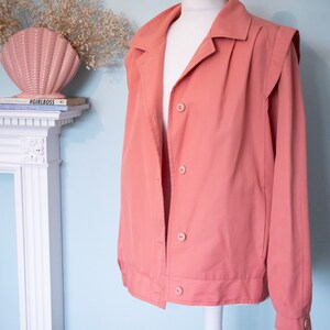 May include: A salmon-colored jacket with a button-up front and long sleeves. The jacket has a collar and a slightly puffed shoulder design.