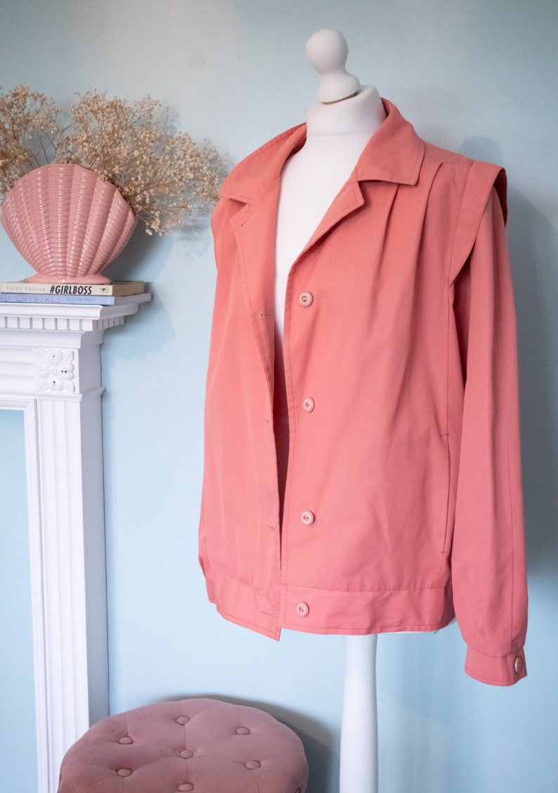May include: A salmon-colored jacket with a button-up front and long sleeves. The jacket has a collar and a slightly puffed shoulder design.