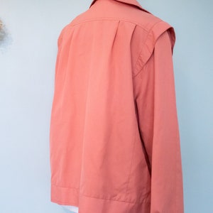 May include: A coral pink long-sleeved jacket with a button closure and a collar.