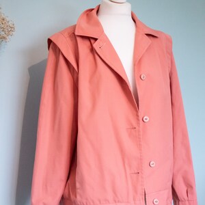May include: A salmon pink jacket with a button closure and a collar. The jacket has a slightly oversized fit and is made of a soft, lightweight fabric.