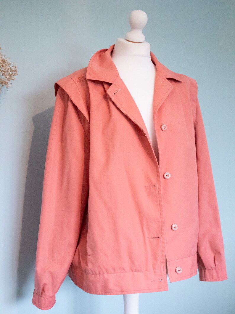 May include: A salmon pink jacket with a button closure and a collar. The jacket has a slightly oversized fit and is made of a soft, lightweight fabric.