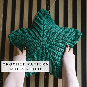 Może przedstawiać: Zielona poduszka w kształcie gwiazdy wykonana na szydełku, trzymana przez dłonie na tle pasiastych wzorów. Pod poduszką widnieje tekst "CROCHET PATTERN PDF & VIDEO".