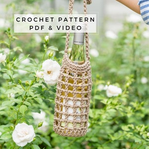 May include: Crochet wine bottle carrier with a tan strap. The carrier is made of beige yarn and has a square grid pattern. The carrier is holding a bottle of white wine.