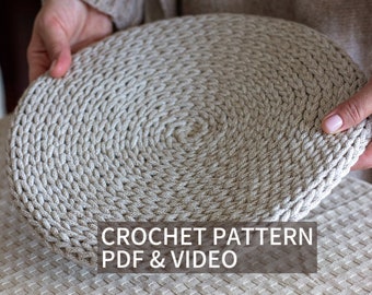 May include: A close-up of a crocheted round coaster in a light beige color. The coaster is being held by a hand. The text "CROCHET PATTERN PDF & VIDEO" is displayed below the coaster.