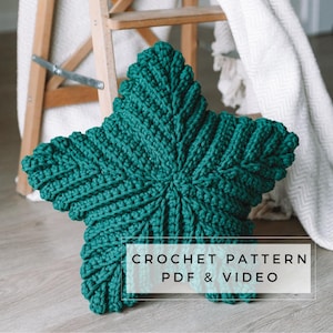 May include: A teal blue crocheted star-shaped pillow with the text "CROCHET PATTERN PDF & VIDEO" on a white rectangle.