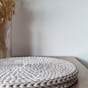 May include: A round, beige crocheted placemat on a wooden table.