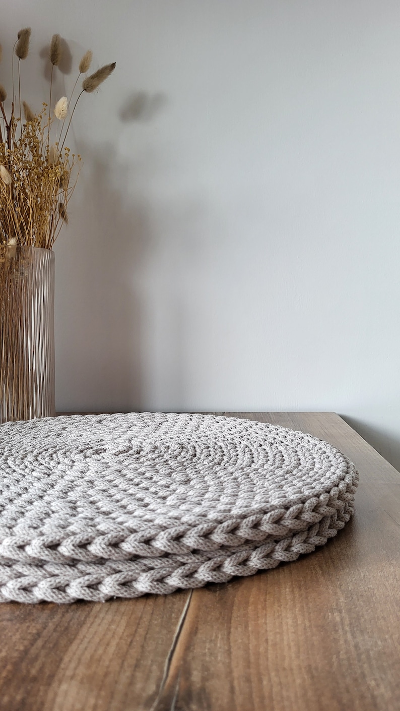 May include: A round, beige crocheted placemat on a wooden table.