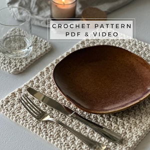 May include: A cream-coloured crochet placemat with a matching coaster, a brown plate, and cutlery. A glass and a lit candle are also present. The text "CROCHET PATTERN PDF & VIDEO" is displayed in a white box.