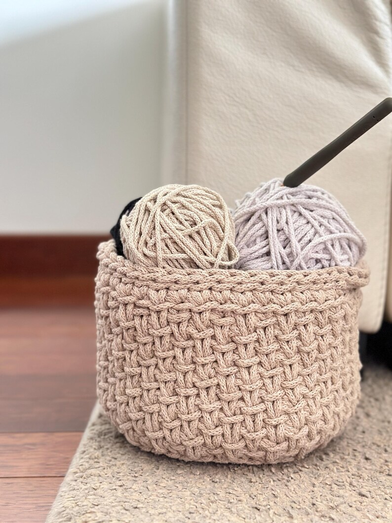 May include: A beige crocheted basket with two balls of yarn inside. One ball of yarn is beige and the other is light purple.