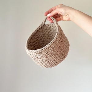May include: A beige crocheted hanging basket with a woven handle.