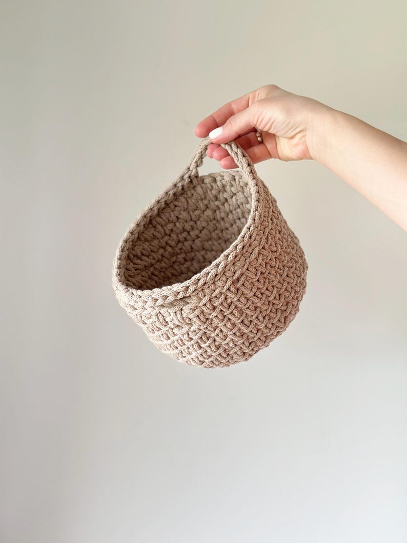 May include: A beige crocheted hanging basket with a woven handle.