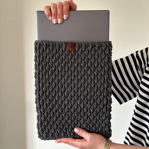 May include: Gray crocheted laptop sleeve with a brown leather button closure.