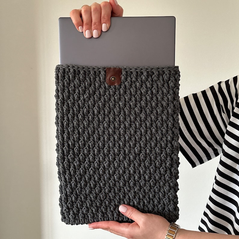 May include: Gray crocheted laptop sleeve with a brown leather button closure.