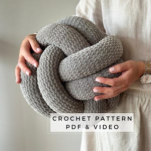 May include: A grey crocheted knot cushion with a text overlay that reads "CROCHET PATTERN PDF & VIDEO".