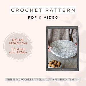 May include: A digital download crochet pattern for a round, white crocheted coaster. The pattern is available in English (US terms) and includes a PDF and video tutorial. The image shows a finished coaster on a table with walnuts.