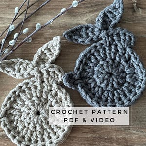 Może przedstawiać: Dwa szydełkowe kształty królików, jeden w kolorze beżowym, a drugi szary, na drewnianej powierzchni. Pod królikami widnieje tekst "CROCHET PATTERN PDF & VIDEO".