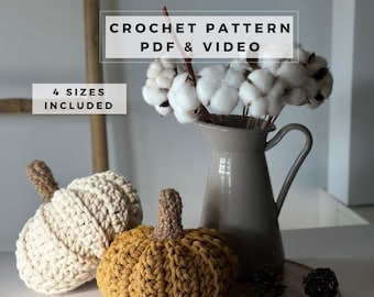 May include: Two crocheted pumpkins in cream and mustard yellow with brown stems, placed next to a gray pitcher filled with white cotton stems. Text overlays read CROCHET PATTERN PDF & VIDEO and 4 SIZES INCLUDED.